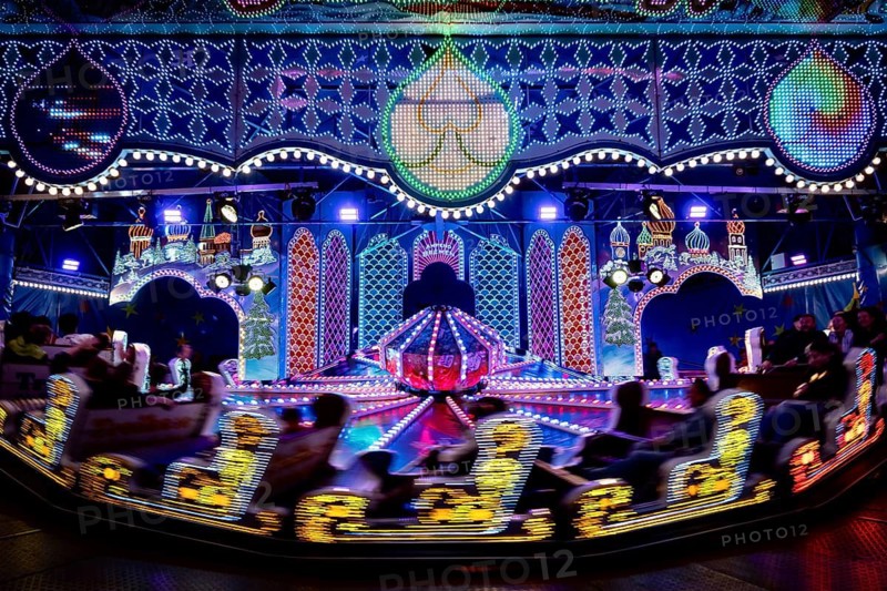 Carousel in neon light, evening at a funfair, Lübeck, Germany