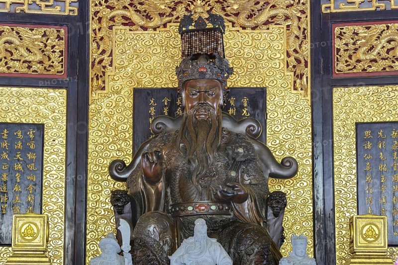 A deity seated majestically on a throne, Shou Xing (also known as Shou Lao or Nanji Xianweng), the god of longevity, carved from dark wood with gold inlays, surrounded by dragon motifs and cloud patterns, symbolises wisdom and long life in Chinese-Daoist culture, Chee Chin Khor Temple, Bangkok, Thailand