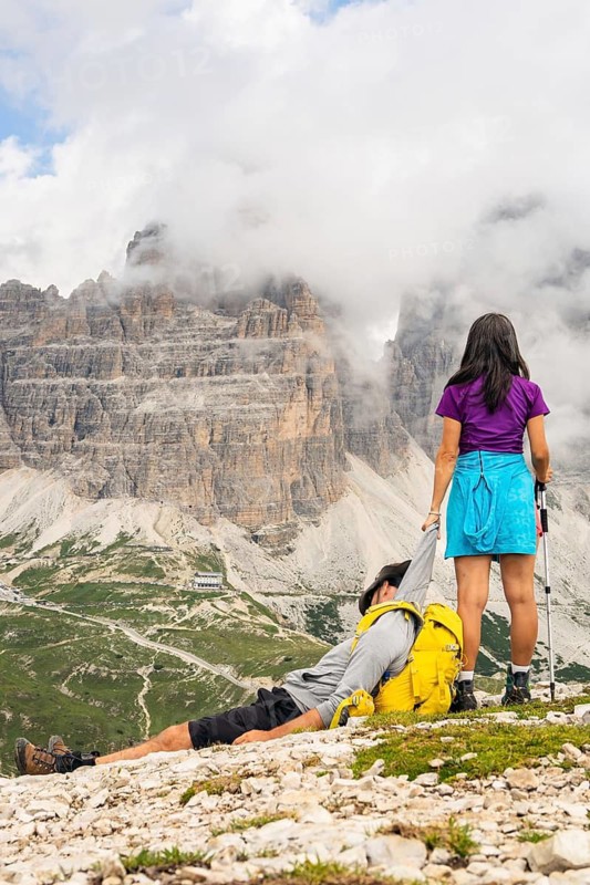 Woman helping exhausted hiking partner boyfriend dragging in Dolomites mountains. Teamwork leadership support trust resilience and shared success moments. Funny meme mock up moments. Italy. Dolomites