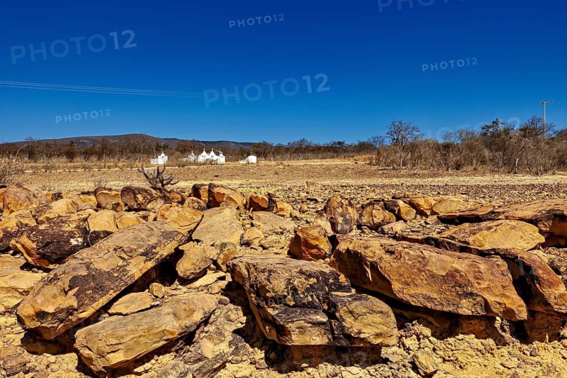 Large rocks lie on the dry, bright desert soil under clear skies, the thornshrub savanna in the Caatinga countryside in the federal states of Pernambuco and Bahia in Brazil