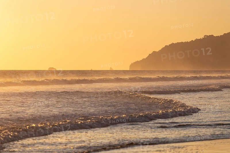 The low sun's golden light illuminates the ocean spray on Carate Beach, with views of Corcovado NP at sunset. Costa Rica