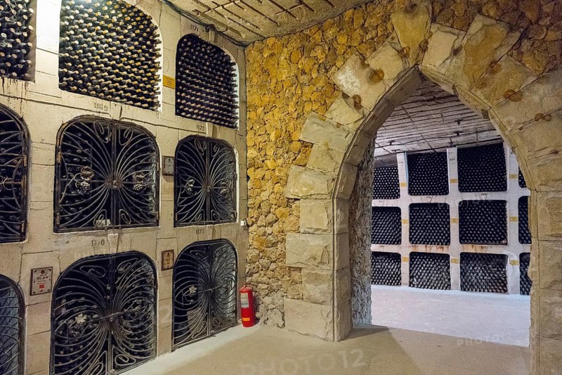 A stone arch separates two sections of a wine cellar filled with wine bottles on shelves, wine cellar, Milestii Mici winery, Mile?tii Mici, Republic of Moldova, Moldova