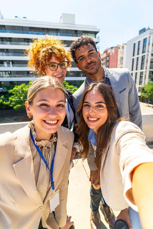 Group of smiling diverse business professionals taking a selfie together on a urban rooftop, celebrating collaboration and success in a modern city environment