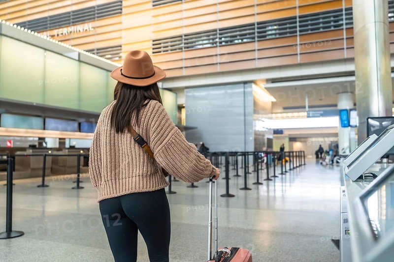Young woman walks through a bright modern airport terminal pulling a suitcase, arriving or departing for a trip, casual traveler with backpack and shoulder bag on a global journey