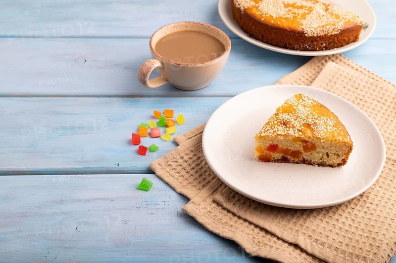 Pie with candied fruit, cup of coffee, on blue wooden background with beige textile, copy space, side view