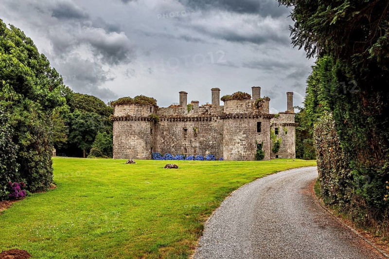 View of an old ruin with round towers from a curved path surrounded by greenery, The ruins of the Château de Kergournadeac'h in Cléder Brittany