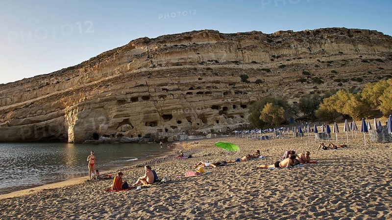 Neolithic caves, former hippie paradise, holidaymakers relaxing on the beach in front of impressive rocks and under umbrellas, Matala, south coast, Crete, Greek Islands, Greece