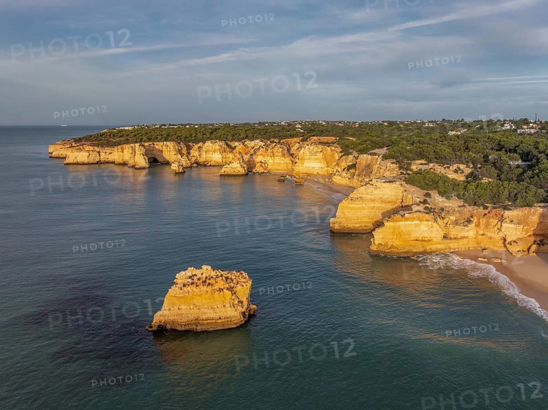 Drone view of Praia da Marinha beach in Algarve, Portugal, with golden cliffs, an offshore rock, turquoise Atlantic water, and a sandy cove
