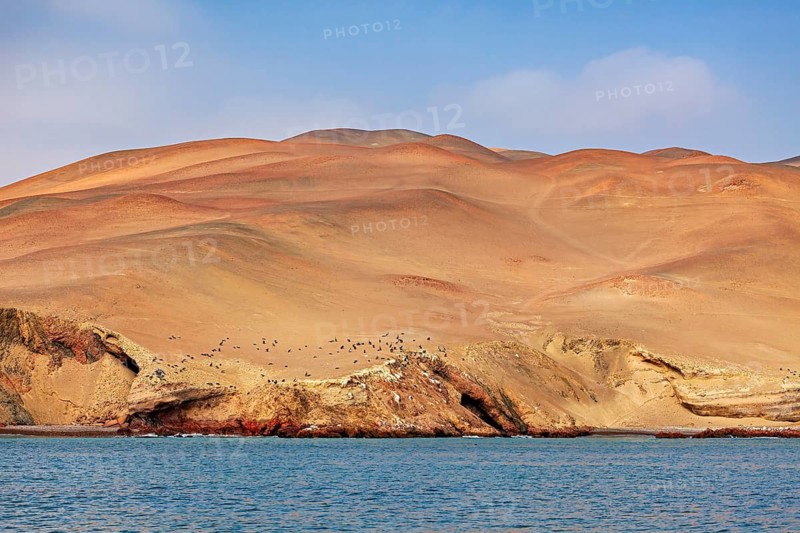 Barren, sandy hills on a coast with blue water under a clear sky, the coast with the desert near Paracas in Peru