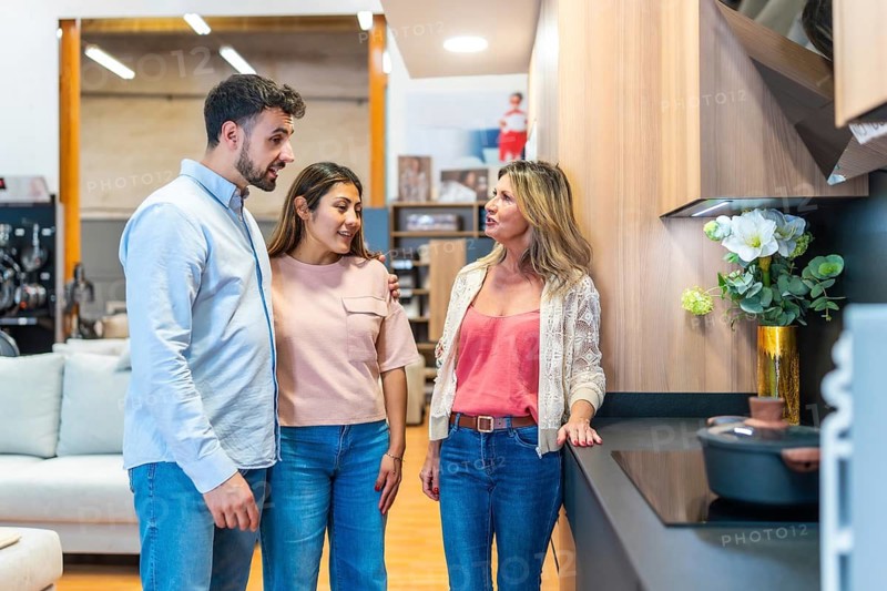 Young couple talking with a female sales consultant in a modern kitchen showroom, exploring different remodeling options and getting expert advice for their home improvement project