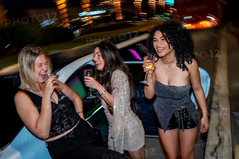 Three diverse young women laughing and drinking sparkling wine glasses, celebrating a special occasion during a luxurious night out with friends in a high end limousine