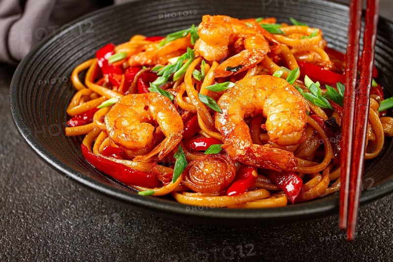 Udon stir-fry shrimp noodles with red bell pepper and green onion, served in a black bowl, with chopsticks, dark background
