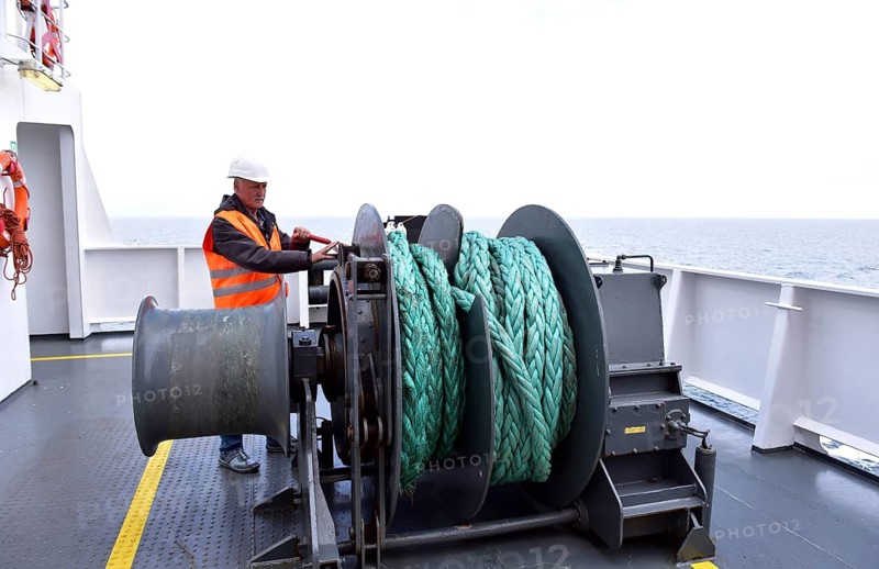 A worker operates a machine on a ship deck with a view of the sea, worker on a tow winch on a container ship, Kiel, Germany