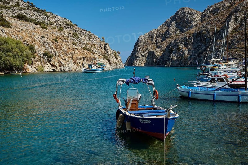 A boat is anchored in clear, blue water between rocky cliffs, Rina, harbour, Vathi, Vathys, Kalymnos, Dodecanese, Greek Islands, Greece