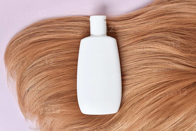 White shampoo bottle on blonde hair with pink background