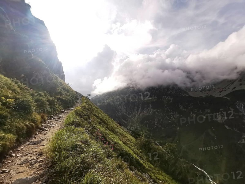 An illuminated mountain trail with dramatic backlight leads through a mountainous landscape, hiking in the High Tatras National Park, Carpathian Mountains, Poland