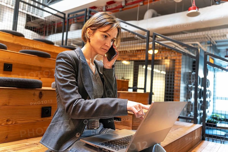 Businesswoman pointing at laptop screen while talking on phone in coworking space