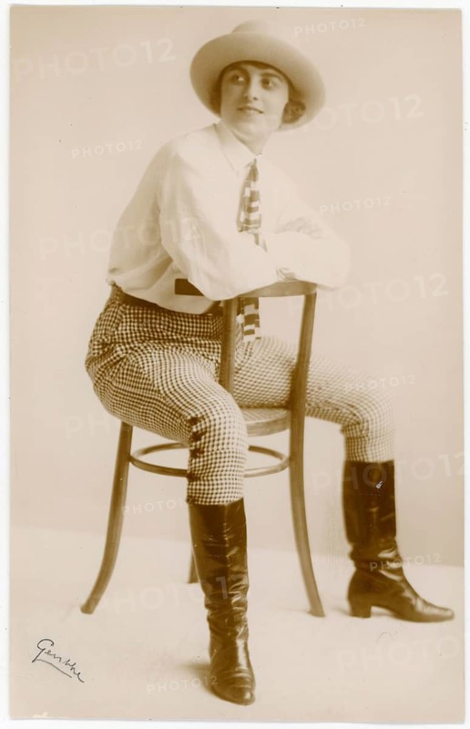 Elegant, self-confident woman in pants, boots, in 1920s clothing sitting on a chair, black and white, Selma Genthe, 1877-1939, around 1926