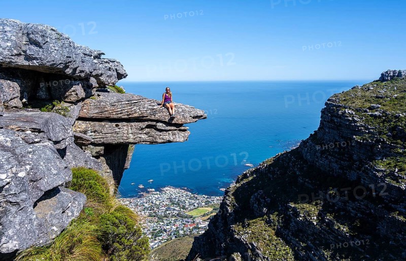 Young woman sitting on an imposing rock pin on a cliff, view of sea and coast, Kasteelspoort hiking, Table Mountains, Eastern Cape, Cape Town, South Africa