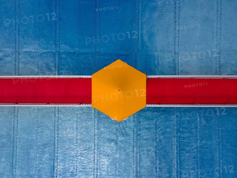 On a red bridge spanning a swimming pool at an open-air lido in Frankfurt, there is a yellow parasol in the centre. The deserted pool below is still waiting for the rush of bathers. The start of the swimming season is just around the corner. (Aerial view taken by drone), Eschersheim, Frankfurt am Main, Hesse, Germany