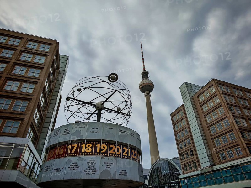 The World Clock and the Berlin TV Tower flanked by modern buildings under a cloudy sky, Alexanderplatz, Berlin