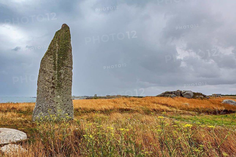 A tall menhir stands out of a grassy landscape surrounded by a cloudy sky. A mood of peace, menhir by Cam Louis, a bronze age megalithic monument in Plouescat, Brittany