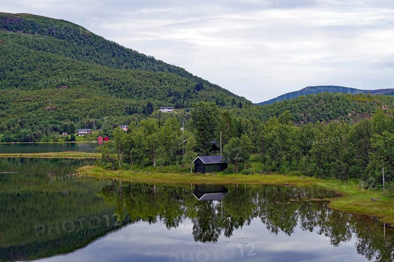 A small wooden building on a quiet lake with forest in the background. Perfect reflection in water, Botnhamm, Troms, Norway