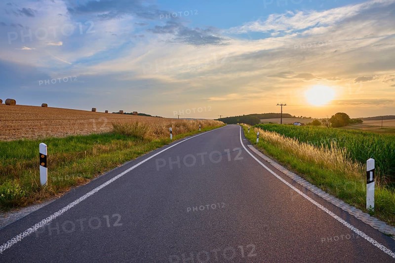 A country road that snakes through the fields as the sun sets on the horizon, summer, Reichartshausen, Amorbach, Odenwald, Bavaria, Germany