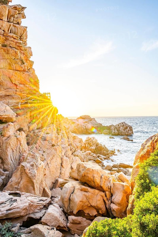 A little trail passing the rocks at the coastline with blue water at Costa Paradiso on a sunny day at sunset, Sardinia, Italy