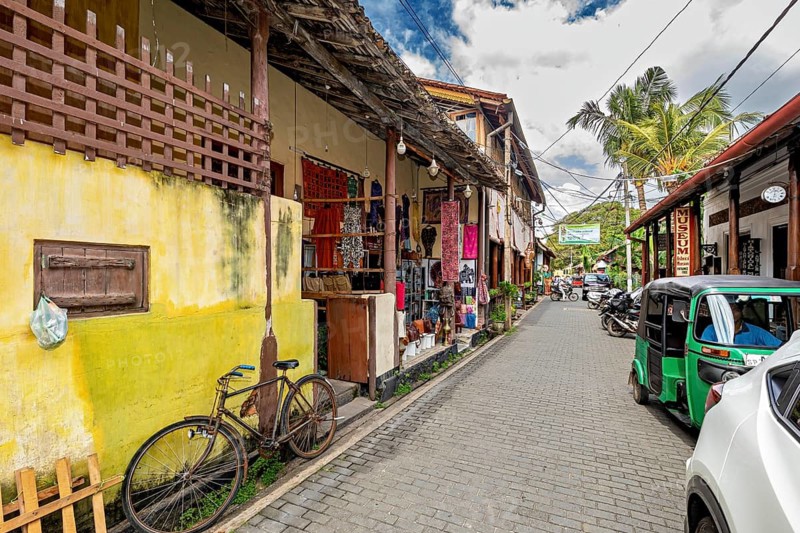 Lively street with colorful shops, a bicycle and tuk-tuks surrounded by tropical plants, the historic downtown of Galle in Sri Lanka
