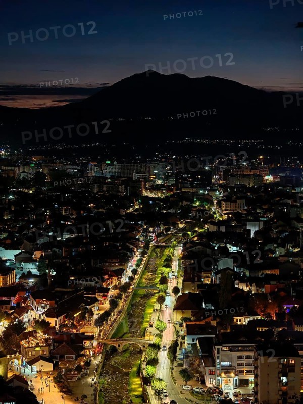 Nighttime cityscape with river, bridges and illuminated roads, hills in the background and dark sky, Prizren, Kosovo