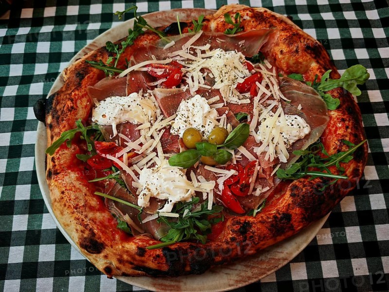 A richly topped pizza with ham, cheese and vegetables on a checkered tablecloth, Croatia