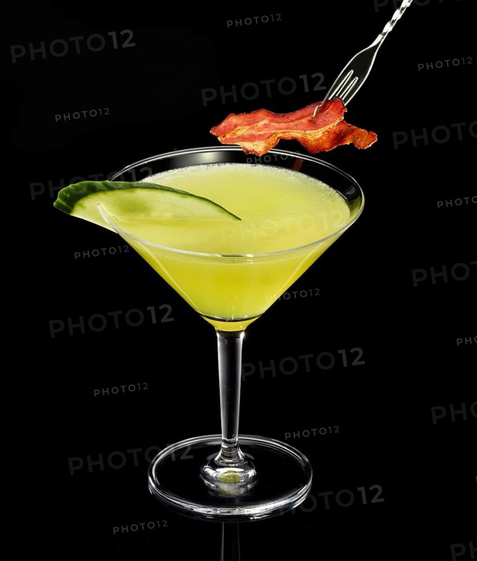 Yellow-green cocktail with black background, cucumber slice and ham as garnish, studio shot