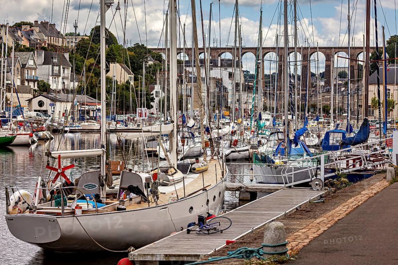 Lively harbor with sailboats in front of a town with a distinctive bridge under cloudy sky, The port of Morlaix in Brittany