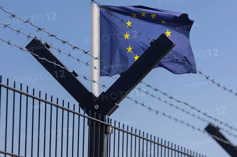 (photo montage) Symbolic image: EU flag behind security fence with barbed wire