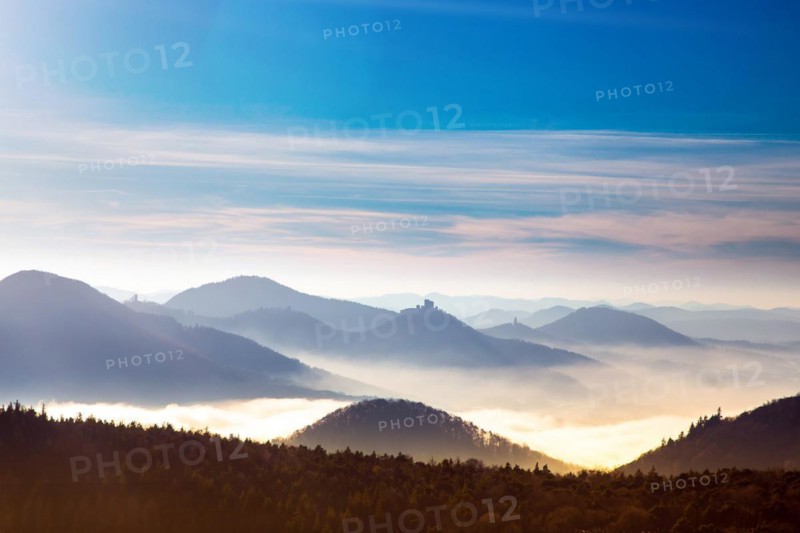 Autumnal panorama of the Palatinate Forest with mountain peaks and valleys in the mist. Trifels Castle near Annweiler can be seen in the centre of the picture