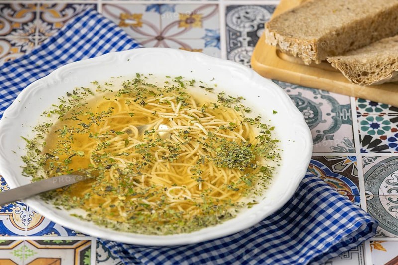 Ready made soup with noodles in a white plate next to bread