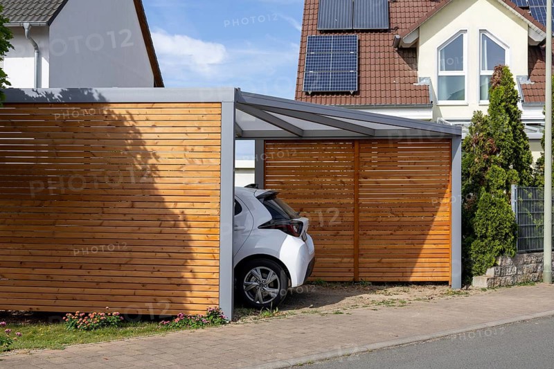 Beautiful carport made of wood and metal with side slatted walls and a fixed roof next to a residential building