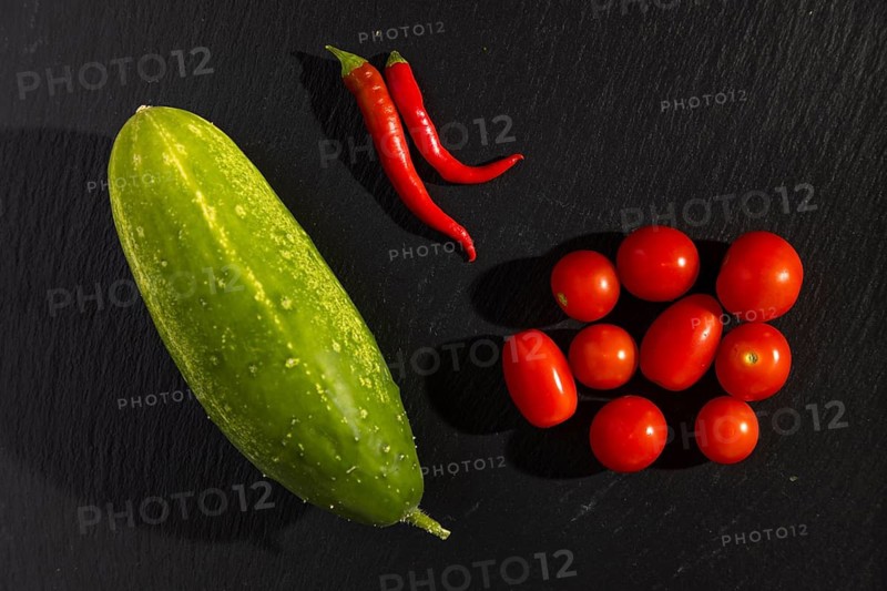 A cucumber, two red chili peppers tomatoes on a dark background