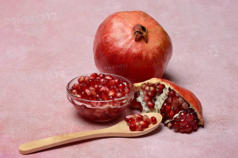 Opened pomegranate and pomegranate seeds in bowl and spoon, Punica granatum