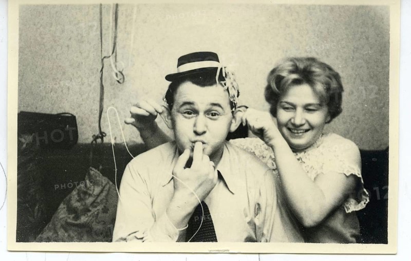 A man wearing a party hat blows impressively streamers while a woman behind him laughs, kaneval, carnival, humor, fun