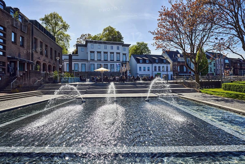 Water features at the town hall, fountain, water basin, general architecture, residential and commercial buildings, catering, outdoor area, paths, lawn, trees, back light, blue sky, veil clouds, cirrostratus clouds, Hafenstraße, Kavarinerstraße, Kleve, Kleve district, North Rhine-Westphalia, Germany