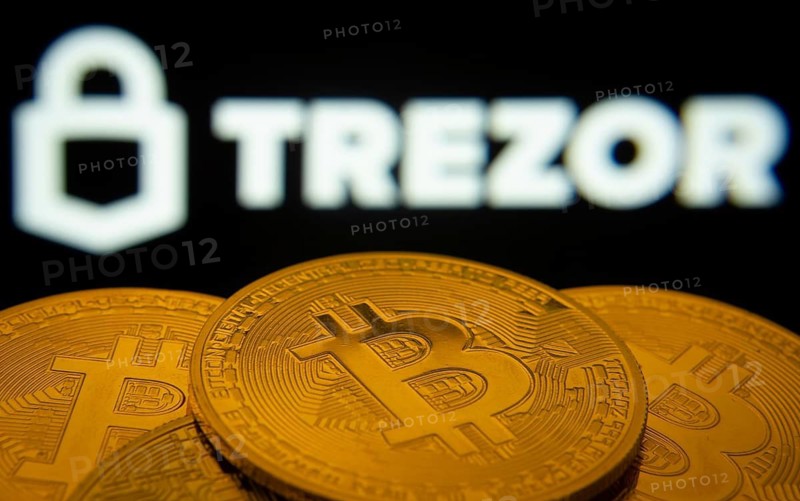 Dhaka, Bangladesh- 30 Sep 2025: Close-up of Bitcoin coins with the Trezor logo visible on a screen in the background