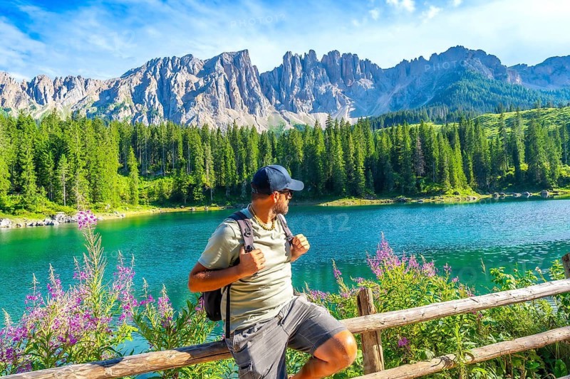 Hiker admiring the stunning turquoise waters of lake carezza, surrounded by the majestic dolomites mountain range in italy, during a sunny summer day