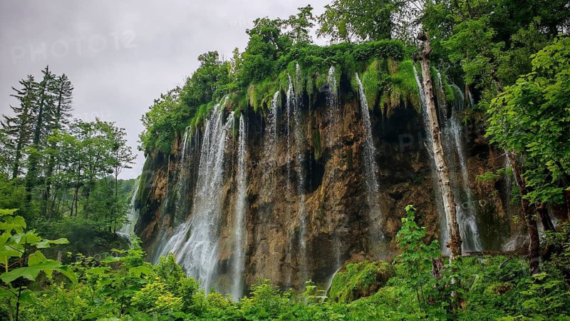 Impressive waterfall falls over steep rocks surrounded by plants, Plitvice Lakes National Park, Croatia