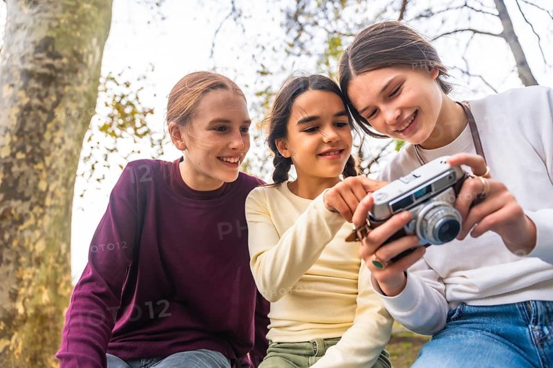 Three happy young siblings spending time outdoors in a park, eagerly looking at a vintage camera and learning about photography, sharing a moment of togetherness and joy