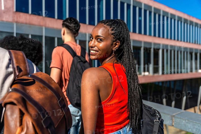Smiling young black student looking back while walking with friends on university campus, representing education, youth, and diversity in a modern academic setting