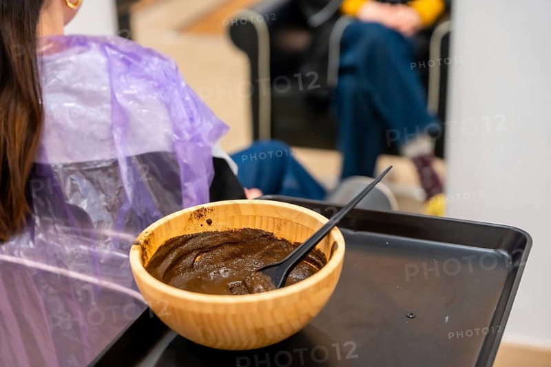 Customer receiving a natural hair coloring application with henna paste from a wooden bowl, focusing on organic beauty and wellness in a salon setting