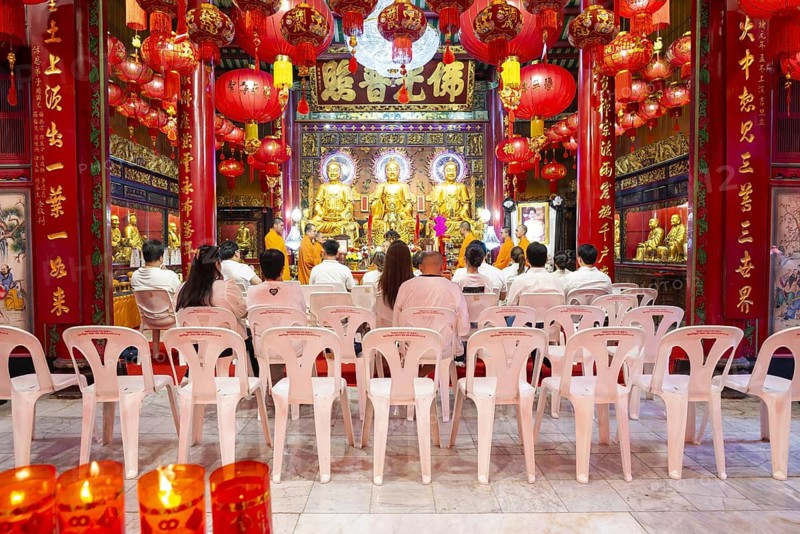 A quiet moment in the heart of a Chinese-Buddhist temple: Three golden Buddha figures shine in warm light, surrounded by filigree ornaments, red inscriptions and offerings that fill the room with an atmosphere of devotion and timeless dignity. The composition of light, gold and ritual objects condenses into a place of inner collection where wisdom, compassion and spiritual presence can be felt. Wat Mangkon Kamalawat, Yaowarat Road, Chinatown, Bangkok, Tailandia