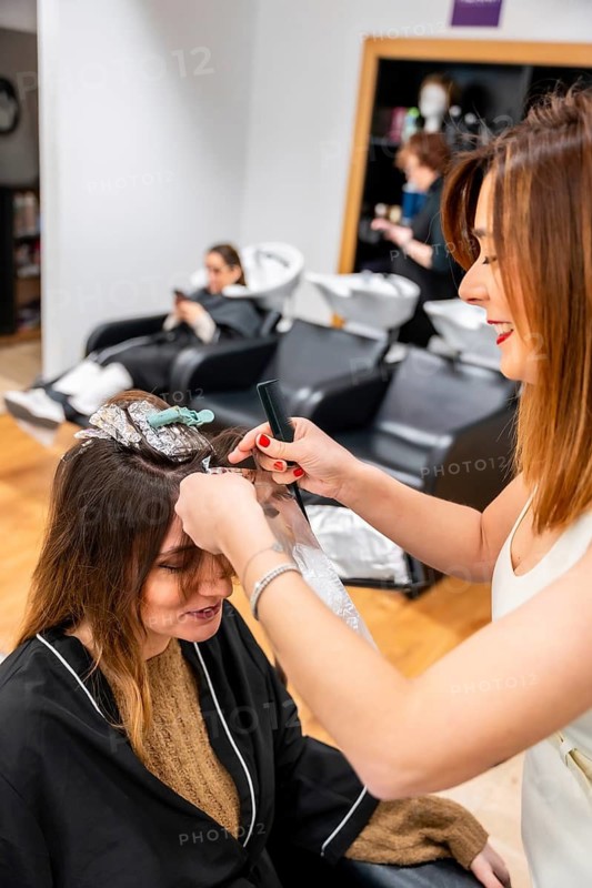 Professional hairstylist delivering a personalized beauty treatment, carefully applying color to sections of a client's hair with foil and a comb, enhancing her look in a modern salon setting